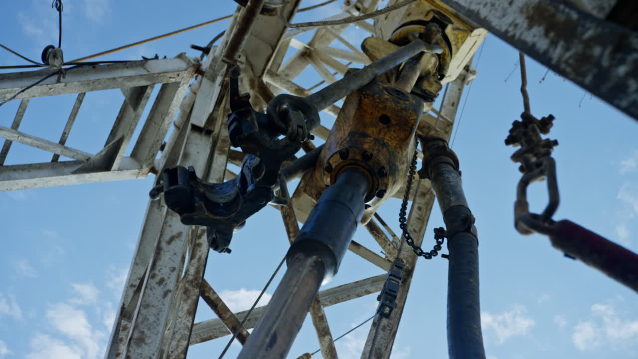 Working equipment with the rotating pole on the metal tower. Low angle view on the machines drilling the oil.