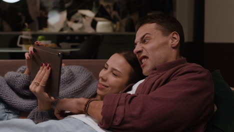 couple relaxing on couch watching tablet