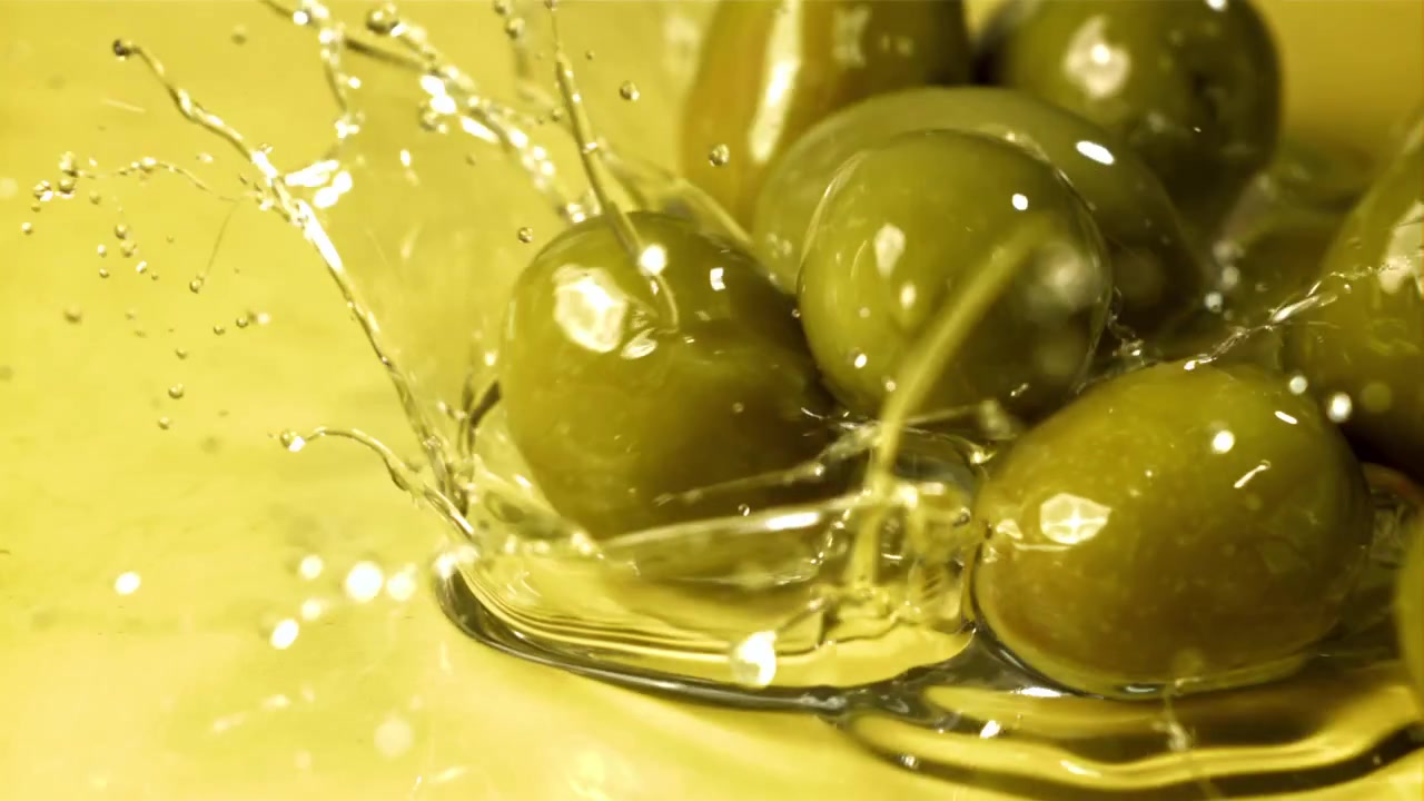 Olive verdi fresche che cadono nell'olio d'oliva dorato al rallentatore.