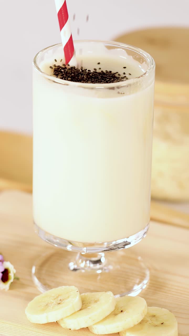 Semillas de chía cayendo sobre un batido cremoso de plátano en un vaso, iluminación brillante, primer plano, toma estática