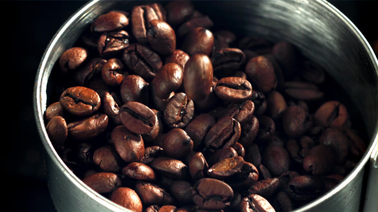 Ristede kaffebønner falder ned i en metalbeholder i slowmotion
