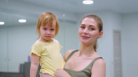 un momento tierno como una madre toca suavemente el cabello de su hija joven mientras ella mira hacia otro lado, ambos en un entorno de gimnasio, esta escena íntima captura un vínculo conmovedor en medio de actividades de fitness