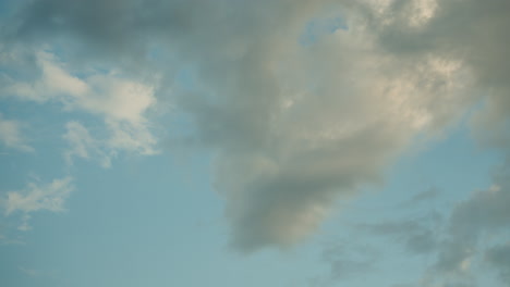 wide shot of sky filled with drifting clouds moving across pale blue backdrop at dusk creating dynamic patterns soft light variations atmospheric mood in expansive aerial scenery sequence