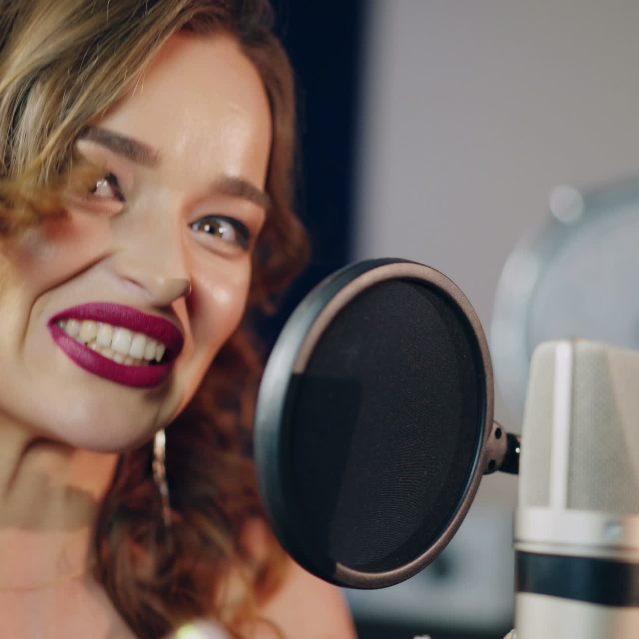 Beautiful face of a singer with bare shoulders singing into a professional modern mic in a recording studio. White and black microphone and a woman. Close-up