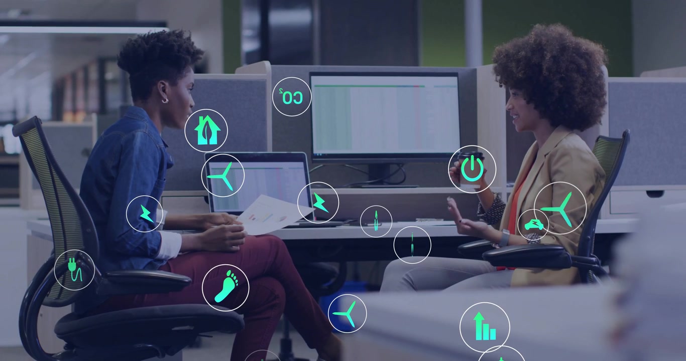 Colleagues using charts and coffee cup at desk initiating glowing tech icons popping amid chat