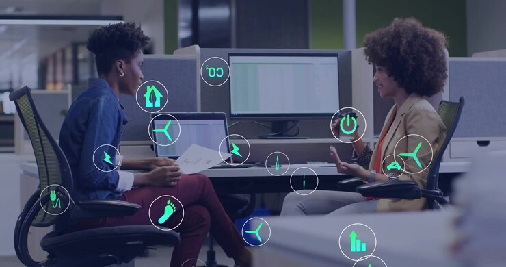 Colleagues using charts and coffee cup at desk initiating glowing tech icons popping amid chat