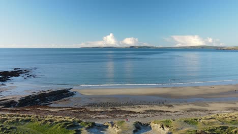 an aerial view over calm ocean, sandy beach and grass covered dunes