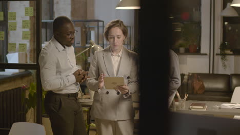 group of three  employees standing in the office, analyzing data on a tablet and discussing marketing strategy together