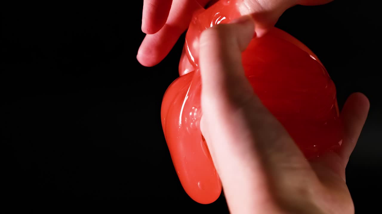 Close-up view of hands stretching and squeezing vibrant red slime against a dark background.