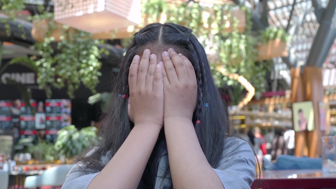 公共の場所で手で顔を覆う少女