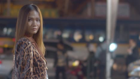 attractive woman does a hair flip, slow motion, to look back at the camera and away from the bight city lights and traffic