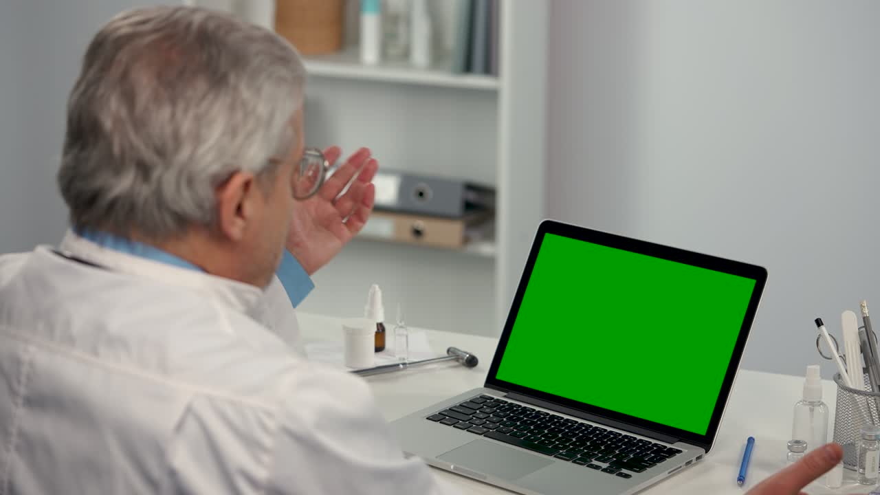 el médico masculino consulta al paciente usando una computadora portátil con pantalla verde y demuestra el vial con la vacuna. consulta remota en línea sobre la necesidad de vacunación. telemedicina. de cerca. cámara lenta