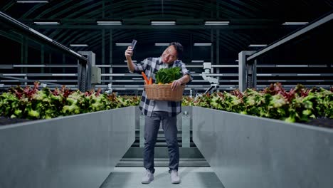 man taking a selfie in a modern vertical farm with a basket of fresh produce