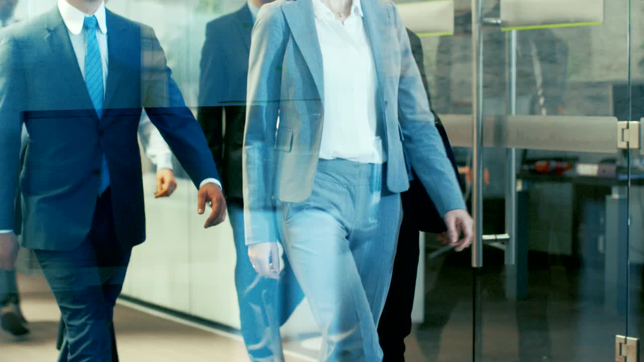 un equipo diverso de delegados o abogados liderados por una mujer marcha con confianza por el pasillo del edificio corporativo. una multitud multicultural de personas de negocios decididas en elegantes oficinas de mármol y vidrio.