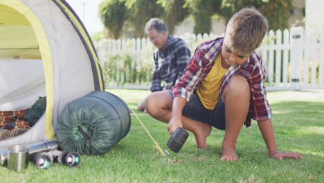 Happy-caucasian-grandfather-and-grandson-pitching-tent-together-in-garden,-slow-motion