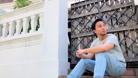 tired young millennial man slowly puts down backpack and sits in front of a wooden gate door at daytime. slow motion
