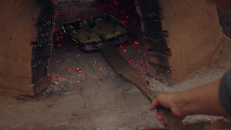 man placing a baking tray with chipas and helping a woman put it inside the tatakua with coals inside