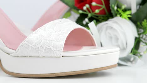 elegant luxury laced bridal wedding shoes and bouquet with red rose on white background closeup