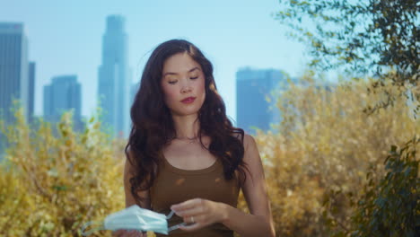 brunette taking off face mask in park. asian girl breathe freely on nature.