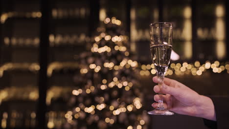 camera focuses on the hand of a woman holding a glass of champagne at the new year's party 1