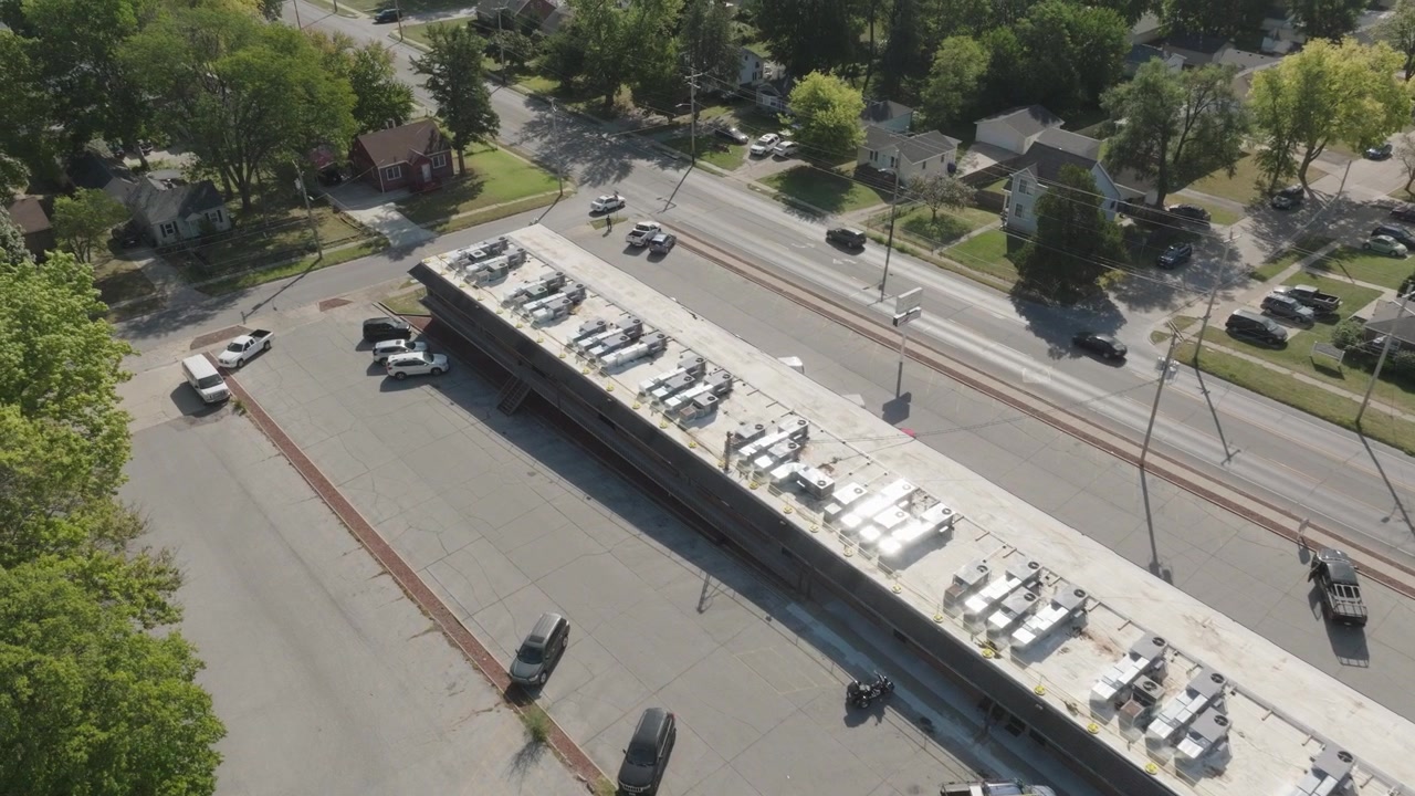 Aerial view of multiple HVAC systems on a flat rooftop of a large commercial building, surrounded by a suburban neighborhood.