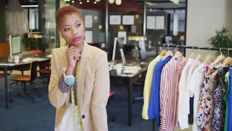 Biracial-businesswoman-thinking-with-clothes-in-background-in-empty-office