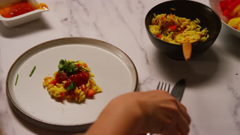 close up of woman at home in kitchen preparing healthy vegetarian or vegan meal sprinkling herbs onto orzo pasta and roasted tomatoes 1