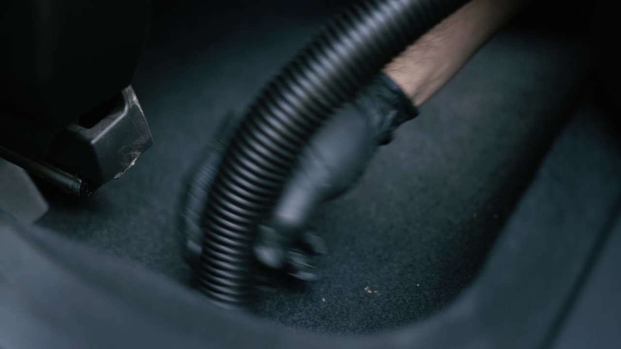 Detail muže v černých rukavicích vysávajícího černý interiér auta.