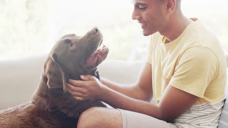 hombre feliz de dos razas acariciando a su perro en casa, cámara lenta
