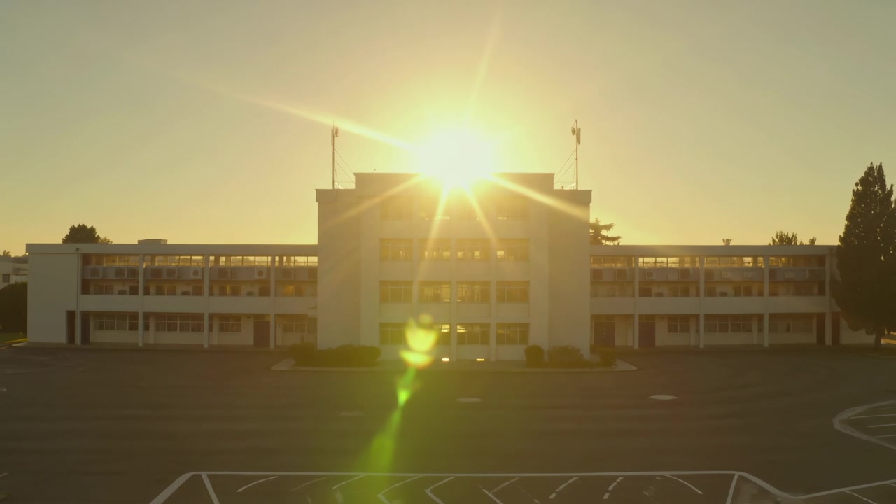 Sol nascente em contraluz em um edifício de três andares no estacionamento, produzindo um reflexo de lente verde vertical.