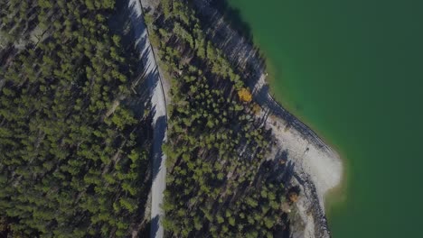 Vista-Aérea-De-Una-Carretera-Rodeada-Por-Un-Bosque-Cerca-De-Un-Lago