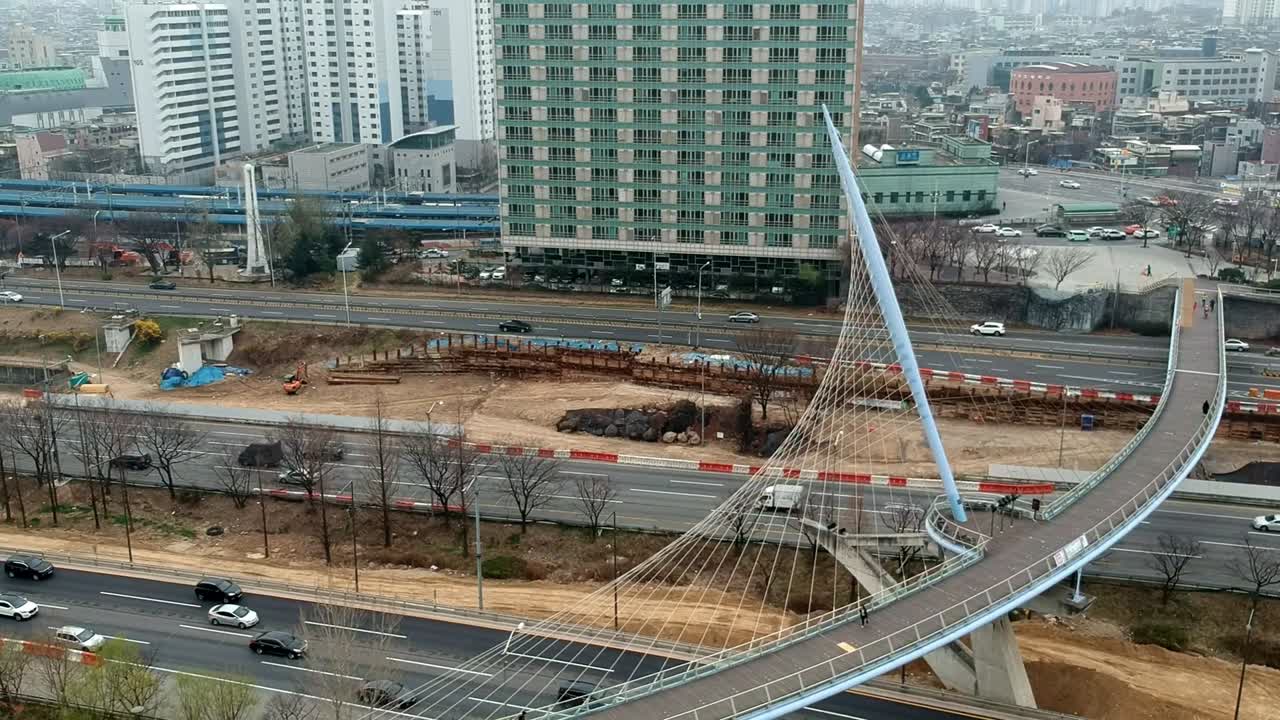 Pull-away shot of a city's traffic filled roads and an artistic pedestrian bridge
