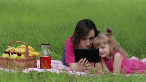 Family-weekend-picnic.-Daughter-child-girl-with-mother-study-lessons-on-tablet.-Distance-education