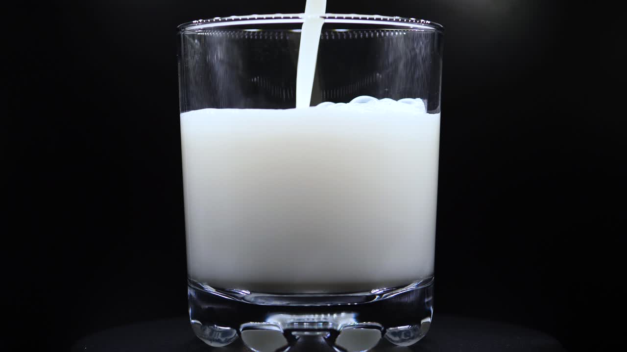verter leche fresca en un vaso transparente de fondo negro