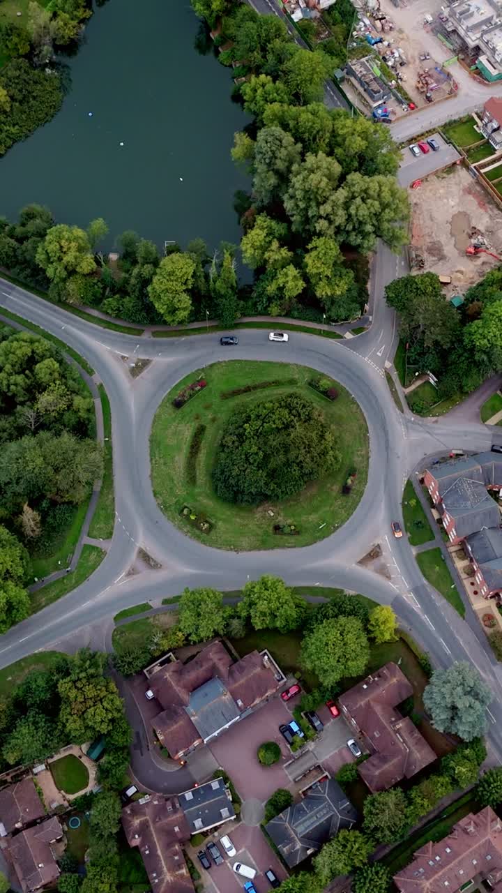 Static portrait aerial drone view over Bishop’s Waltham roundabout and pond, capturing moving cars, autumn trees, and warm golden sunset light across the peaceful village town setting