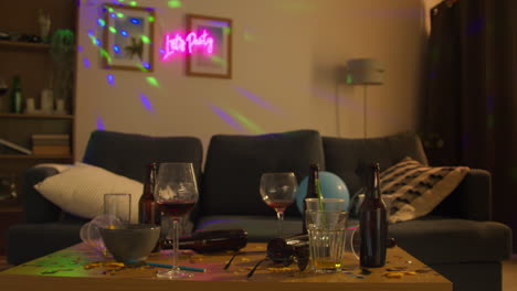 salón desordenado o sala de estar con mesa cubierta con vasos de vino vacíos y botellas de cerveza después de la fiesta de la casa
