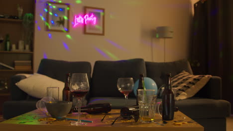 messy lounge or living room with table covered with empty wine glasses and beer bottles after house party