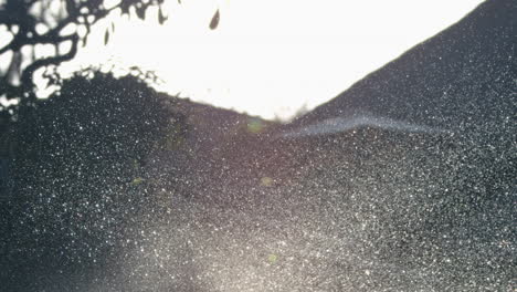 sprinkler water spray in slow motion, mist rolls over dark lawn as light filters through
