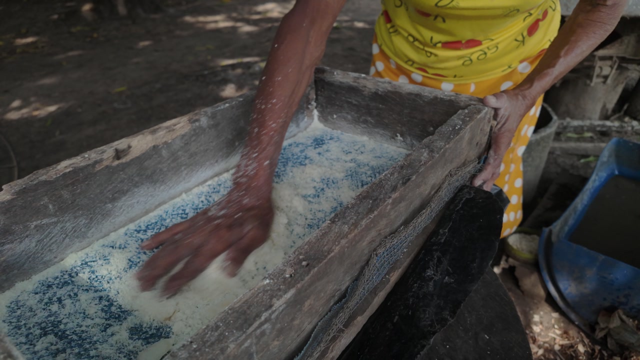 Elderly woman sifting cassava flour for traditional bread outdoors