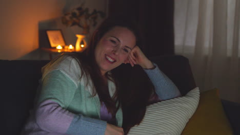 smiling woman sitting on sofa at home at night streaming or watching movie or show on laptop 3