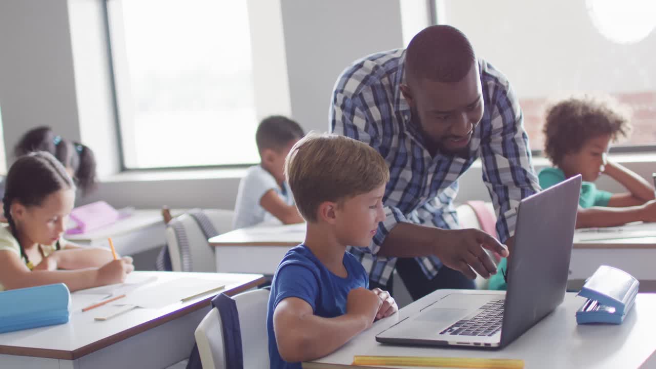 Video of happy african american male teacher helping caucasian boy with laptop