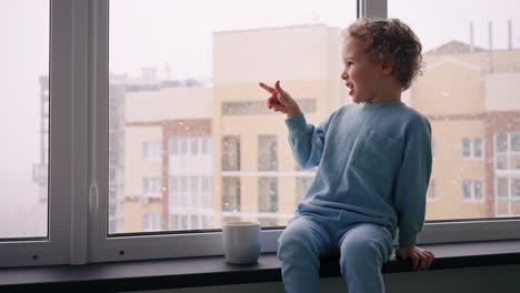 curious little child is looking out window and amazing by snow christmas miracle and cozy atmosphere in home