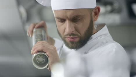 portrait of chef cooking at kitchen. concentrated chef peppering food.