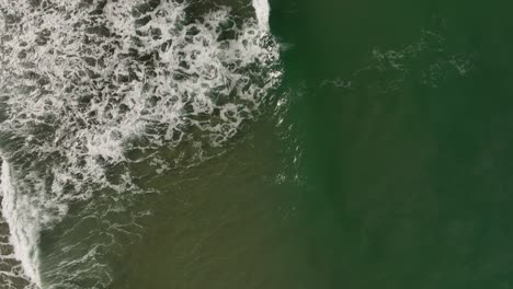 Overhead-aerial-tracking-waves-breaking-along-seaside-shoreline