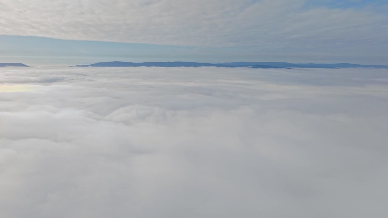 A panoramic aerial view rising above a sea of clouds with mountain peaks in the background