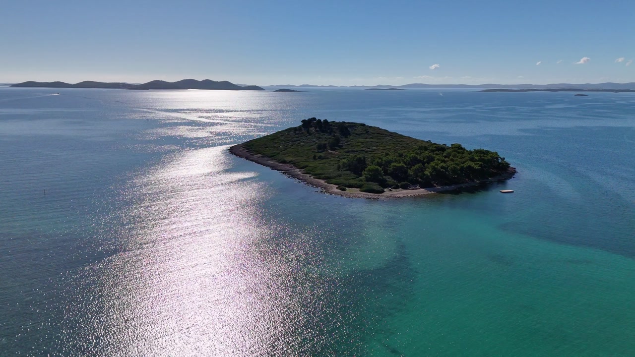 Drone liftoff on a sunny October day near the island in front of Pakoštane, with the Adriatic shimmering in the sunlight as the camera rises over the blue sea.