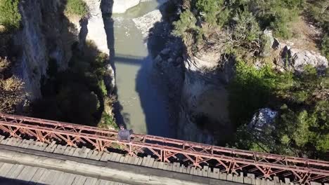 Sobrevuelo-De-Un-Ser-Humano-Sentado-En-Un-Viejo-Puente-De-Madera-Oxidado-Sobre-El-Cañón-De-Osumi-Cerca-De-Corovode-En-Albania