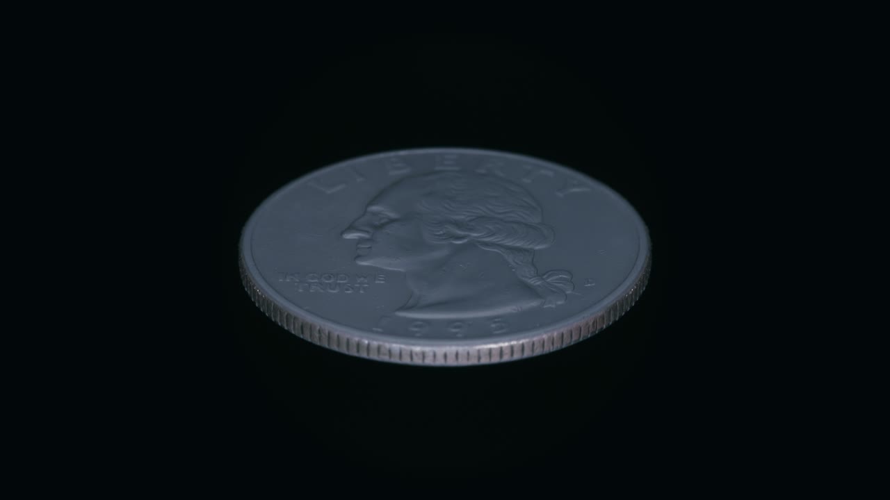 sobre un fondo negro, una moneda de un cuarto de dólar está en rotación y brilla en los rayos de luz.