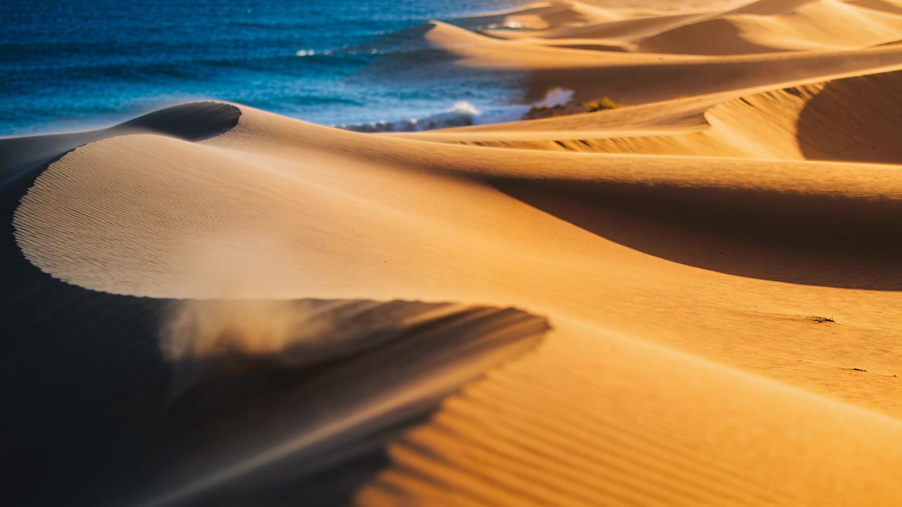 Una transizione che spinge toni caldi attraverso una duna a mezzaluna sulla costa, fondendo la metà fredda dell'oceano nelle creste.