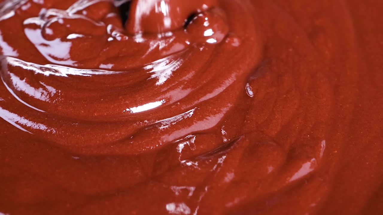 A detailed view of glossy chocolate being swirled, showcasing its rich texture and fluid motion.